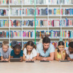Teacher and kids lying on floor using digital tablet